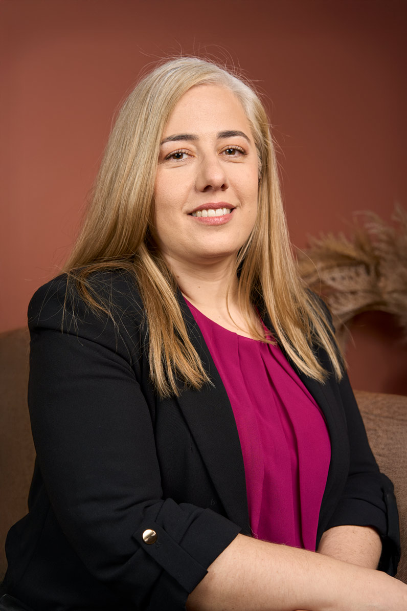 Portrait corporate d'une collaboratrice blonde souriante en blazer noir et haut fuchsia sur fond terracotta, Paris