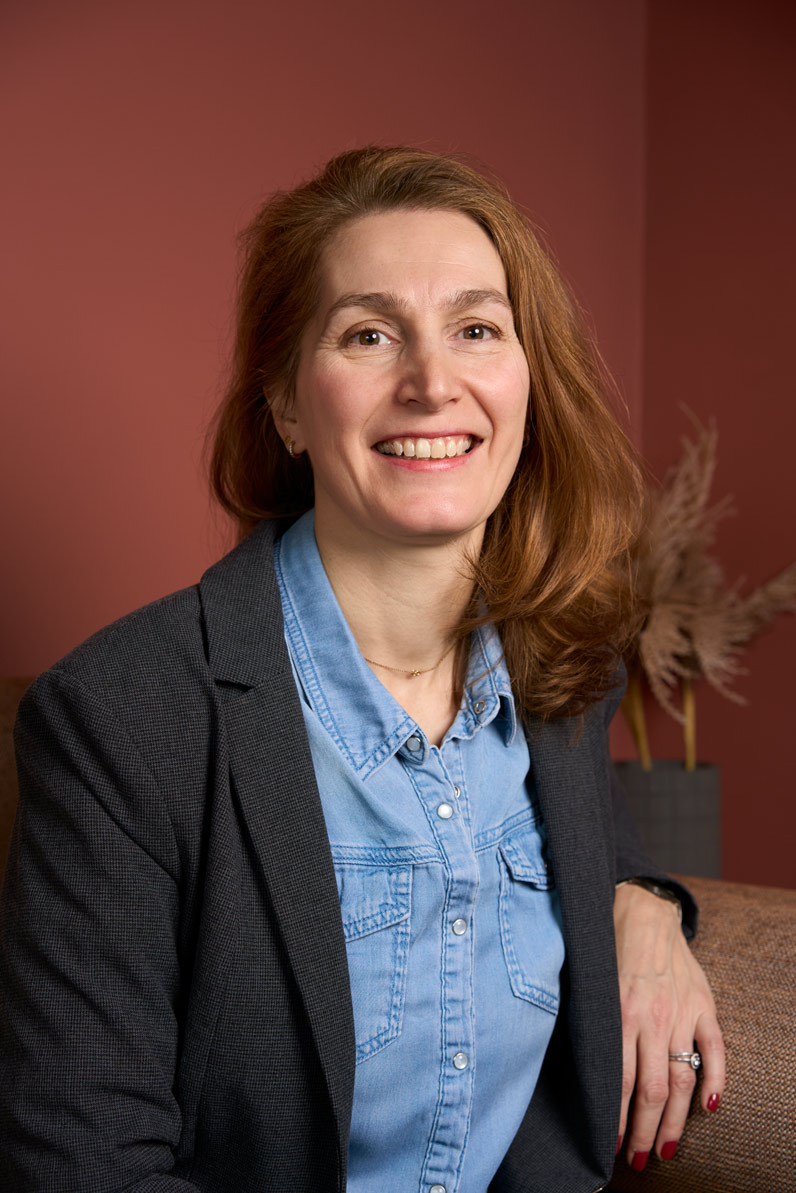 Portrait corporate d'une professionnelle de la formation souriante en tenue smart casual (chemise en jean et veste) sur fond terracotta, Paris