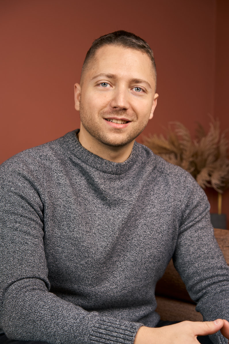 Portrait corporate d'un collaborateur en tenue décontractée (pull gris) sur fond terracotta, shooting équipe Paris